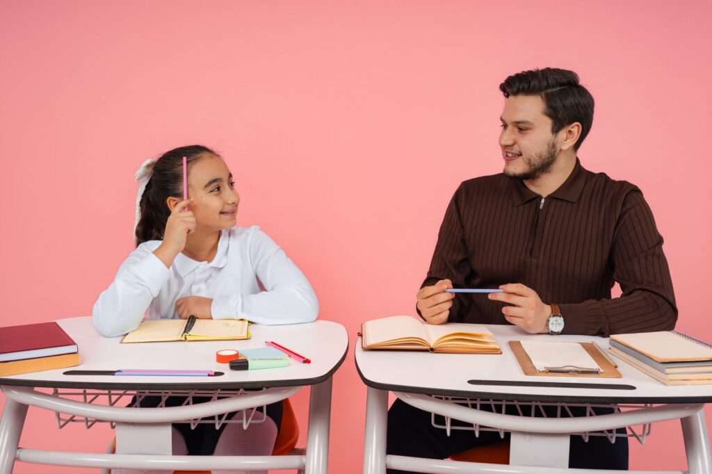 A teacher and a pupil sitting together at school desks during a lesson