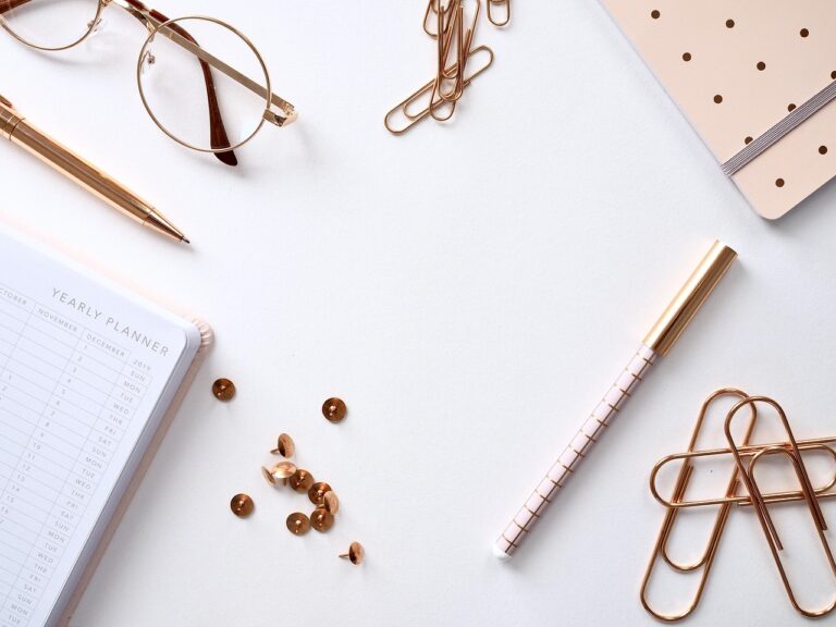 A flat lay of desk items: glasses, a planner, a pen and paperclips