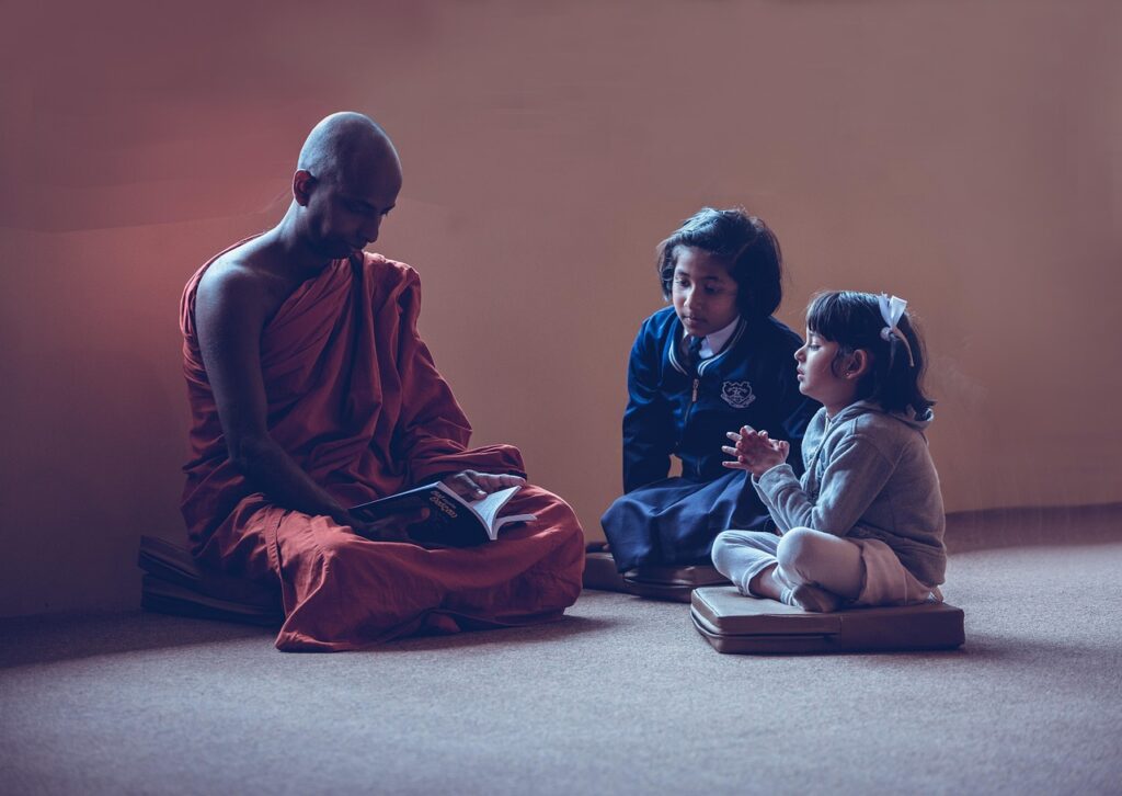 An adult sitting cross-legged, talking calmly with two seated children
